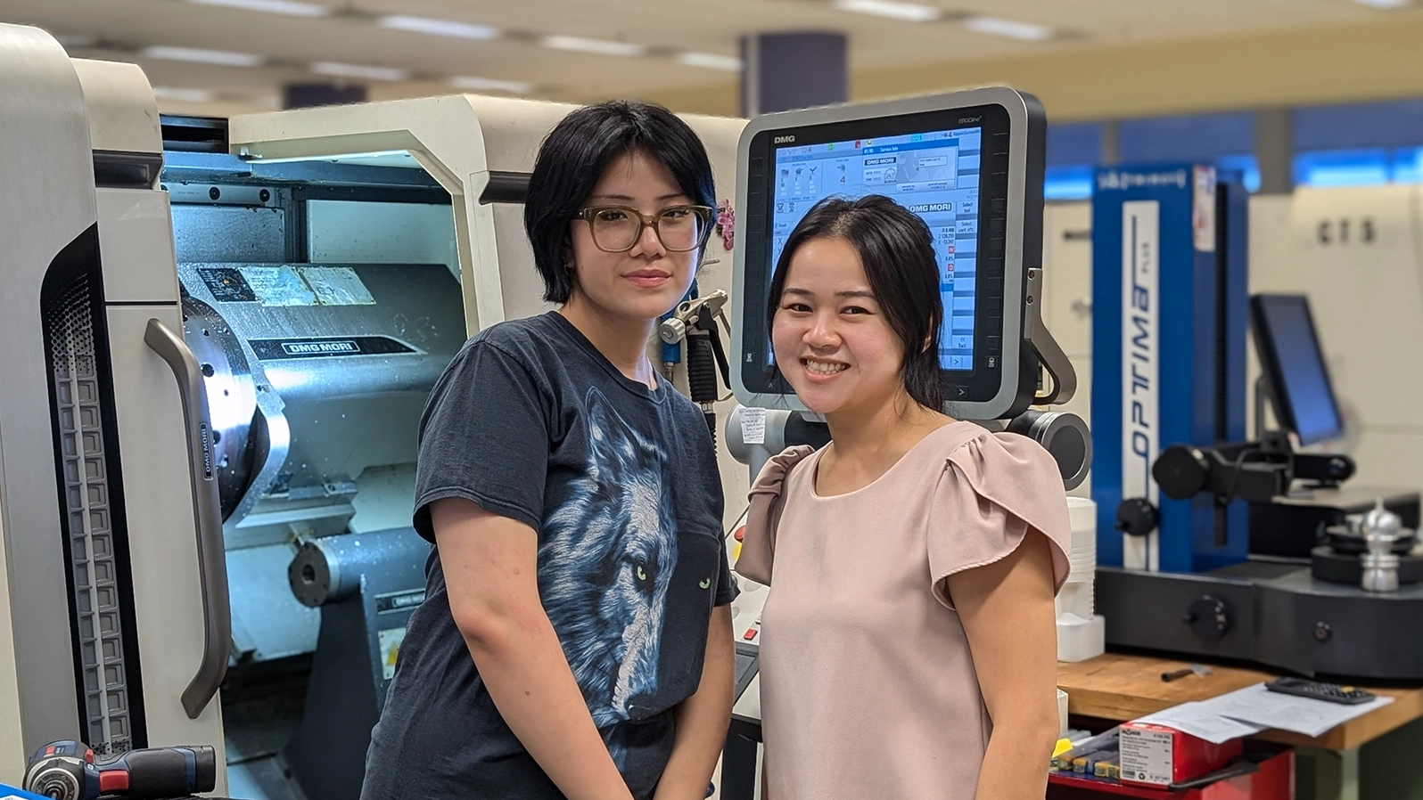 Eunice and Jia Xin stands in the middle of a lab set-up, surrounded by multiple equipment.